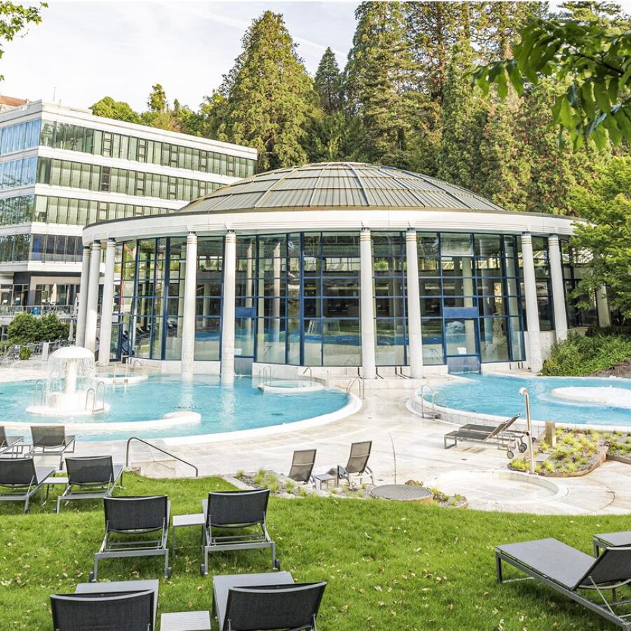 Außenansicht der Caracalla Therme in Baden-Baden mit Glasrotunde, Außenbecken und umliegender Liegewiese mit Sonnenliegen.